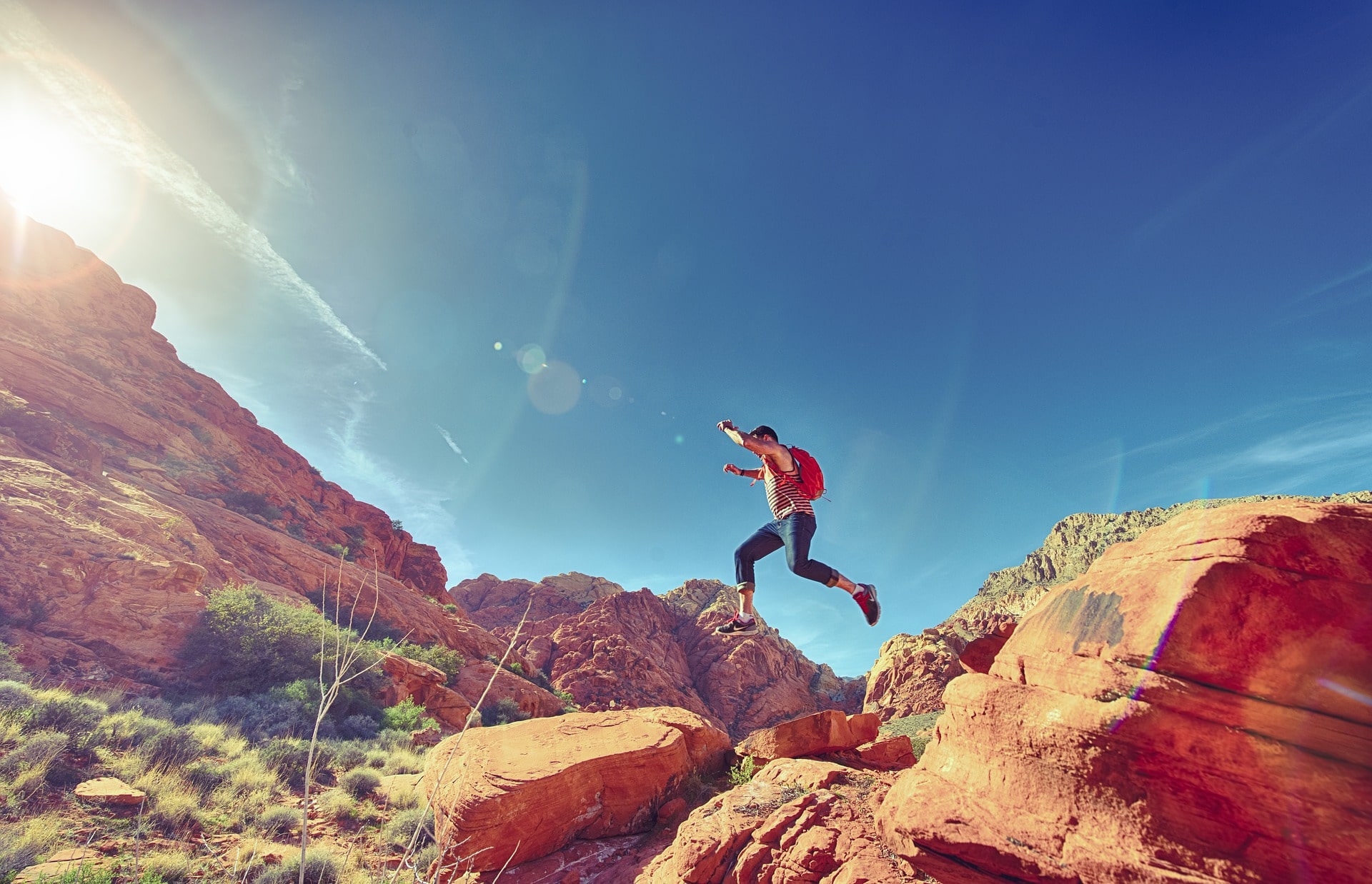 A person is running on top of rocks in with the sun blaring down on him
