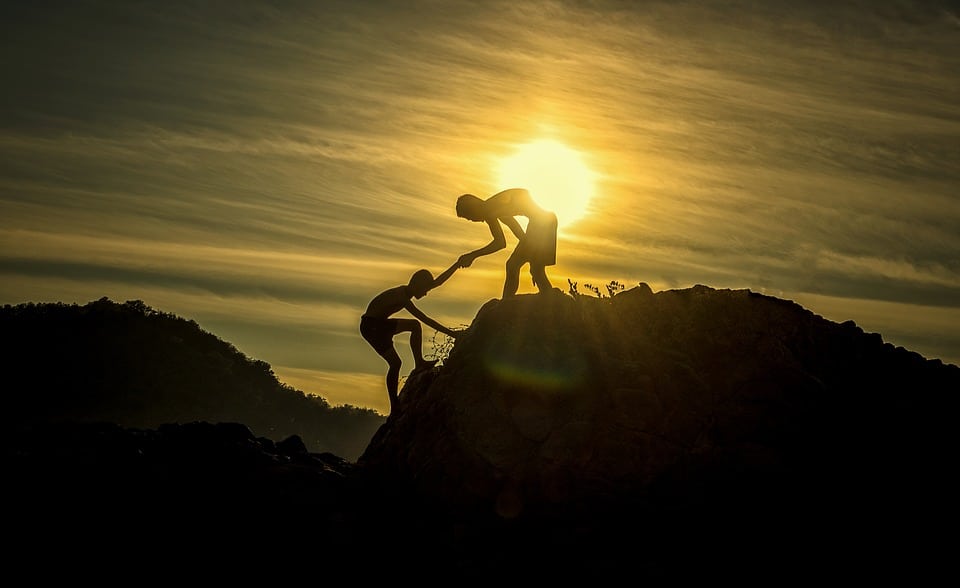 Two people on top of a mountain helping each other up behavior change