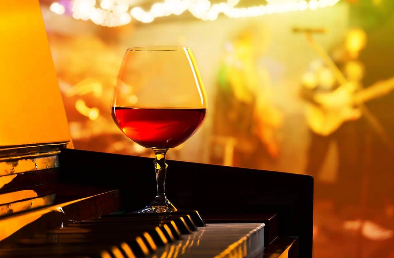 A glass of red wine on a table with a band in the background