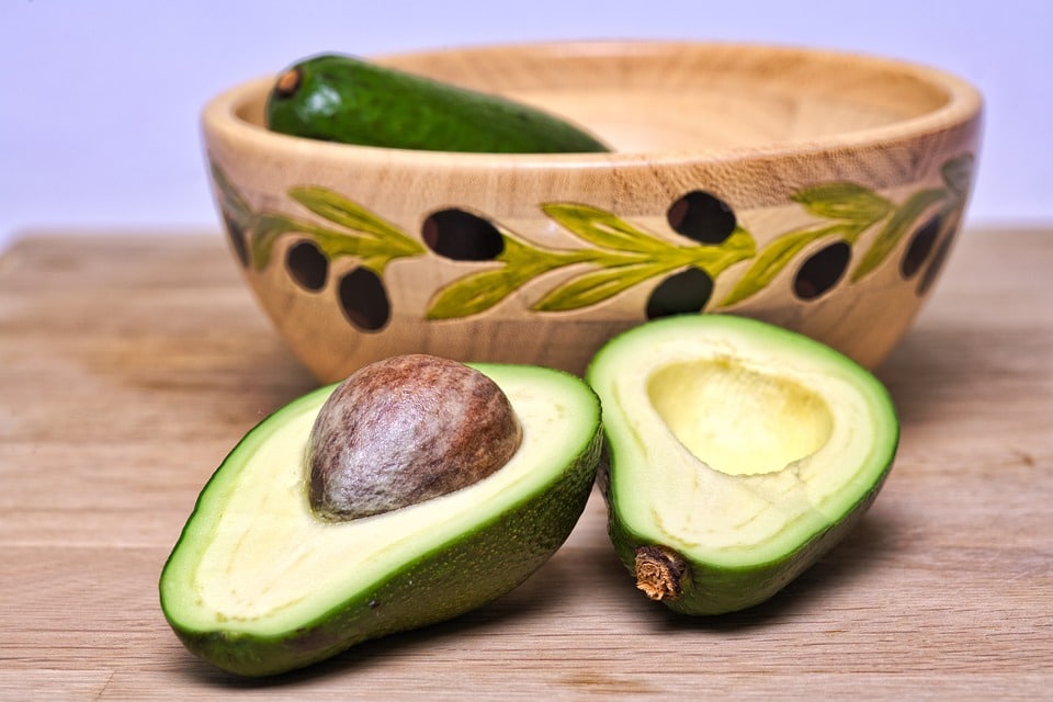 A avacado is sliced in half and sitting in front of a bowl heart disease