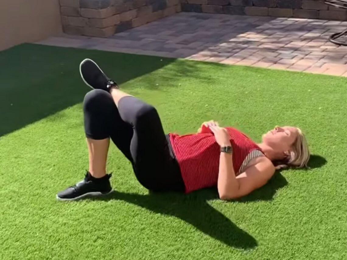 A woman lying down doing a full body workout in her backyard