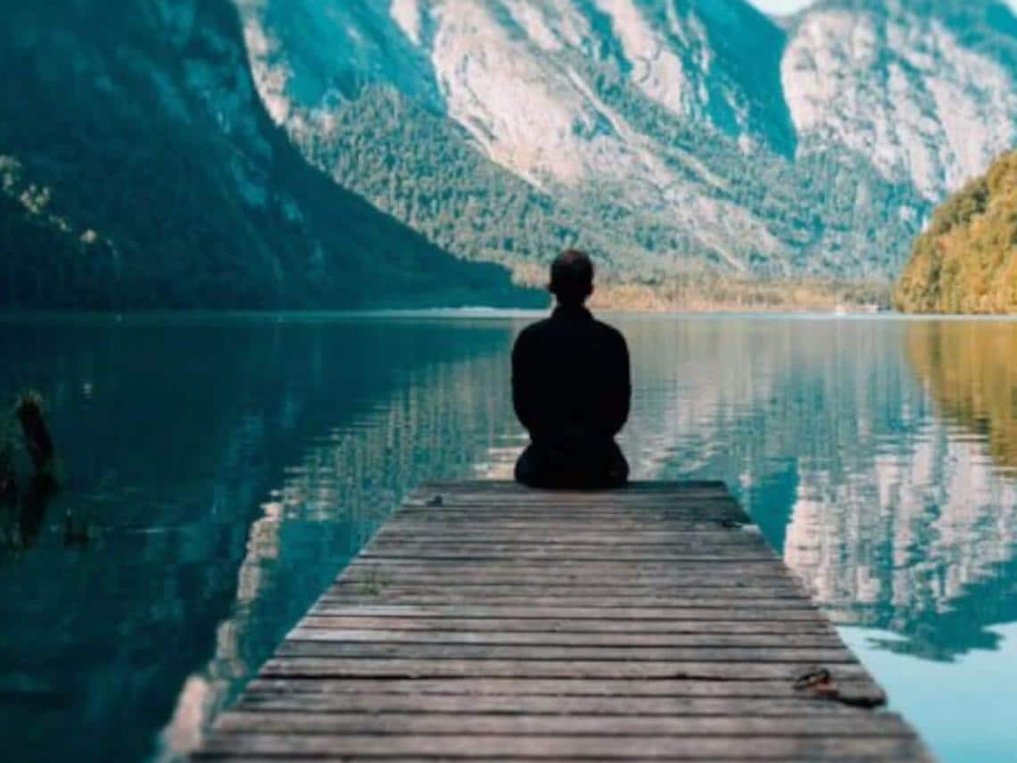 A person meditating on a dock with a scenic view of the mountains