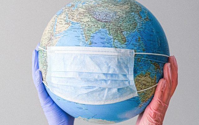Globe wearing mask with gloved hands holding it up, trash